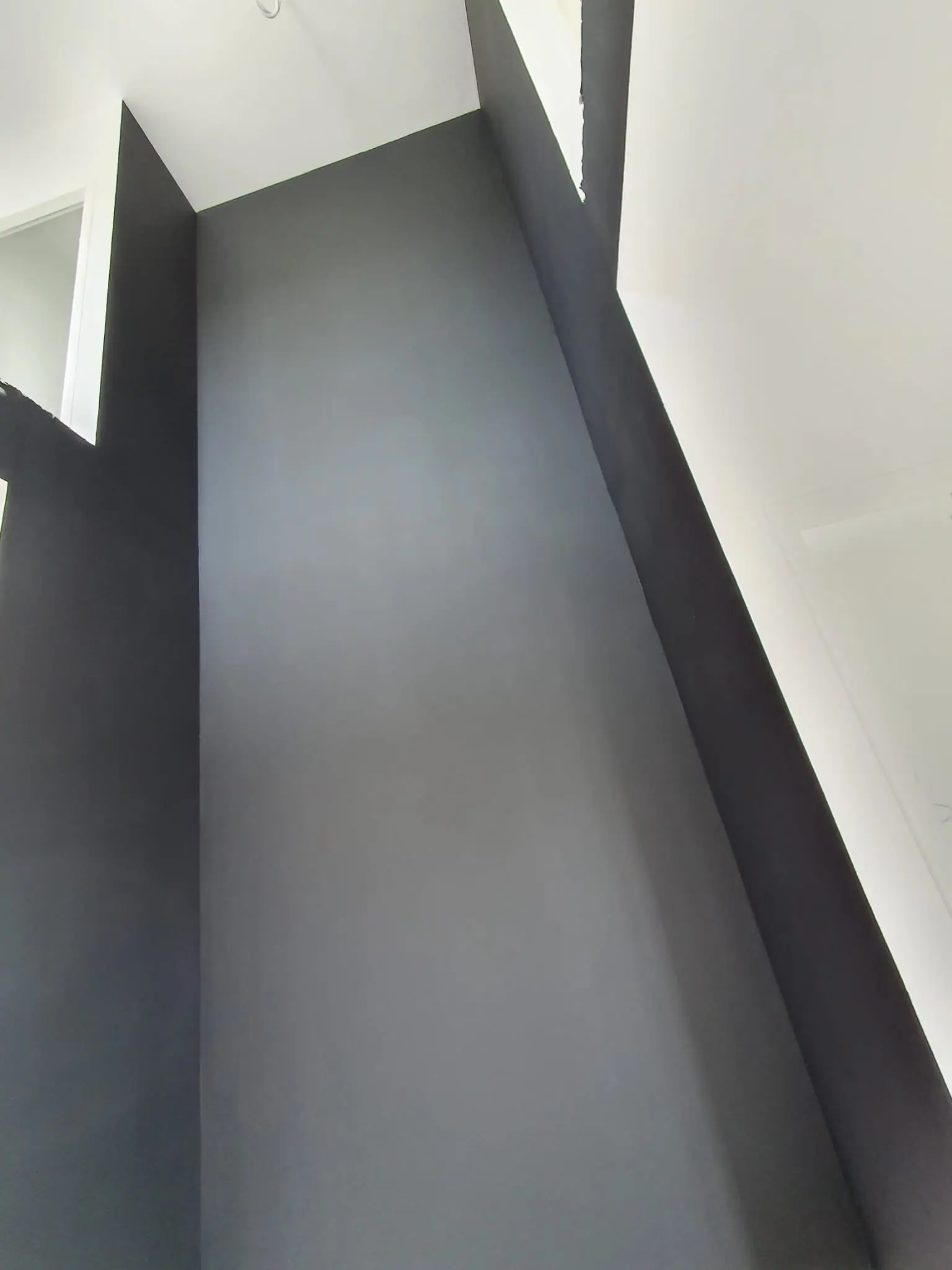 Mur toute hauteur peint en gris anthracite mat, entre un plafond et des murs blancs