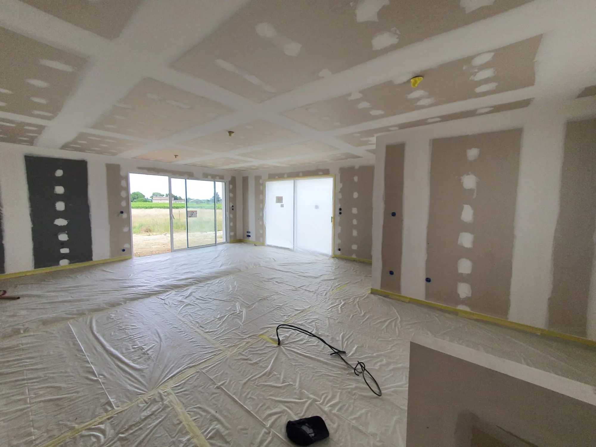 Maison neuve en finition : joints de plaques de plâtre enduits, sol entièrement bâché, baie vitrée ouverte sur les vignes