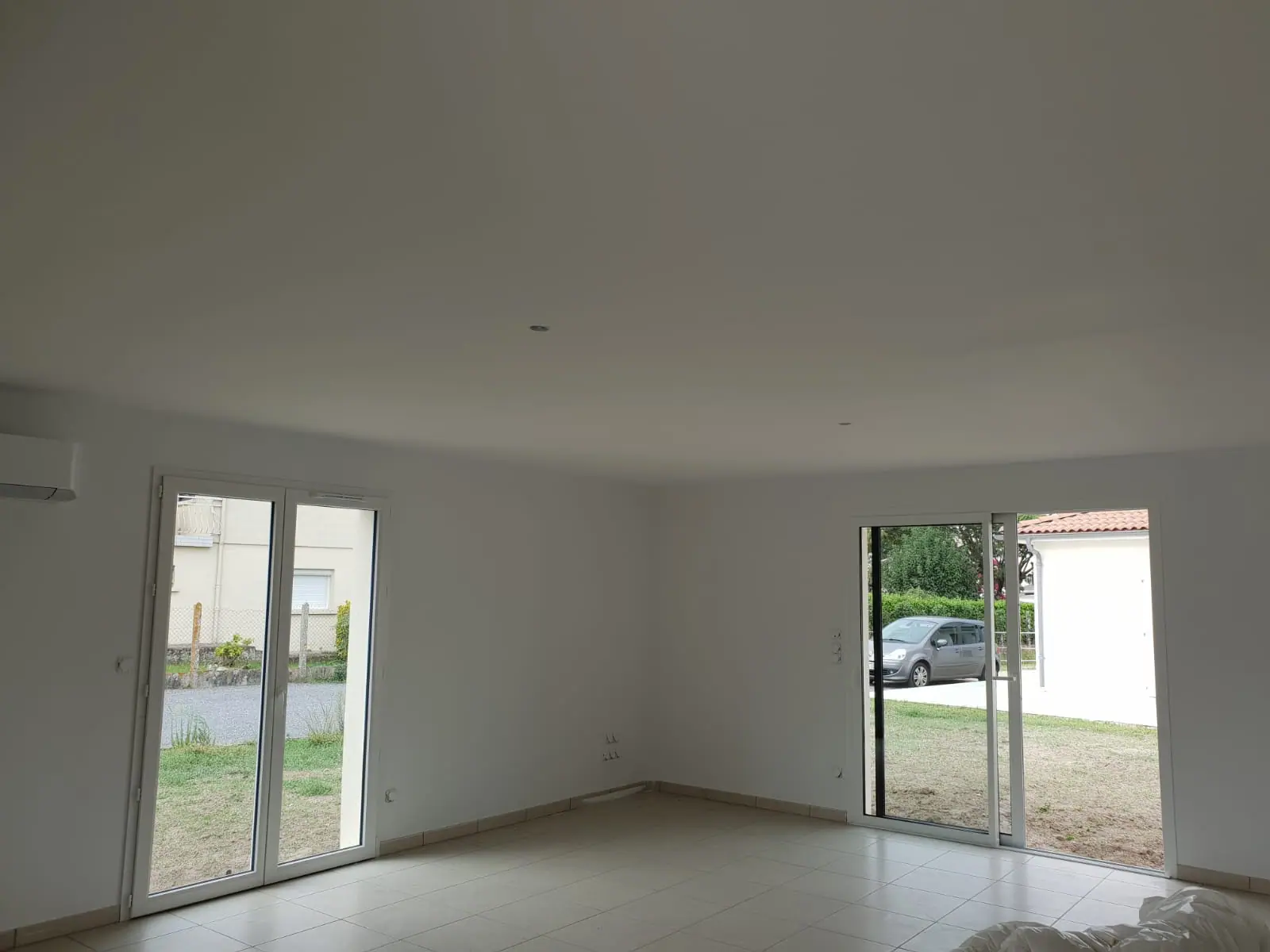 Après : le même séjour aux murs et au plafond blancs, carrelage clair et baie ouverte sur le jardin