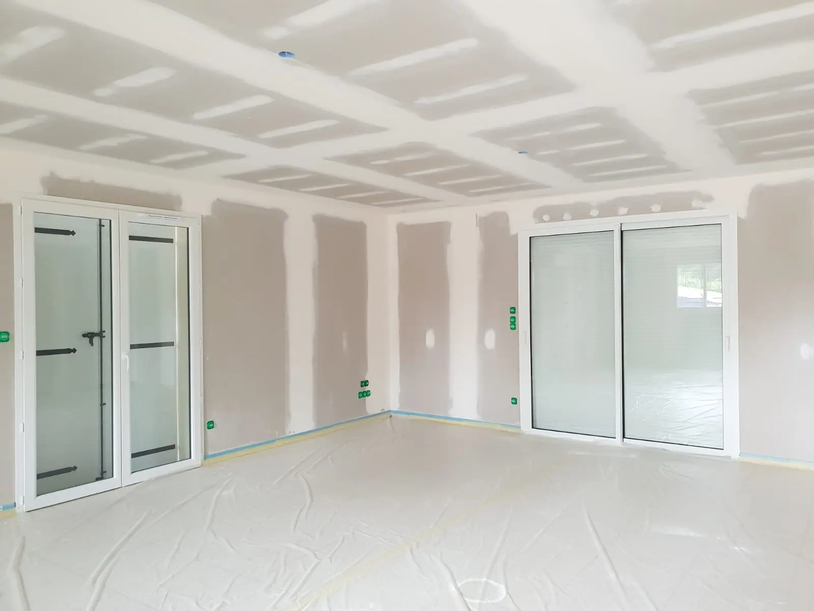 Avant peinture : séjour de maison neuve aux plaques de plâtre jointées, porte-fenêtre et baie coulissante, sol protégé par une bâche