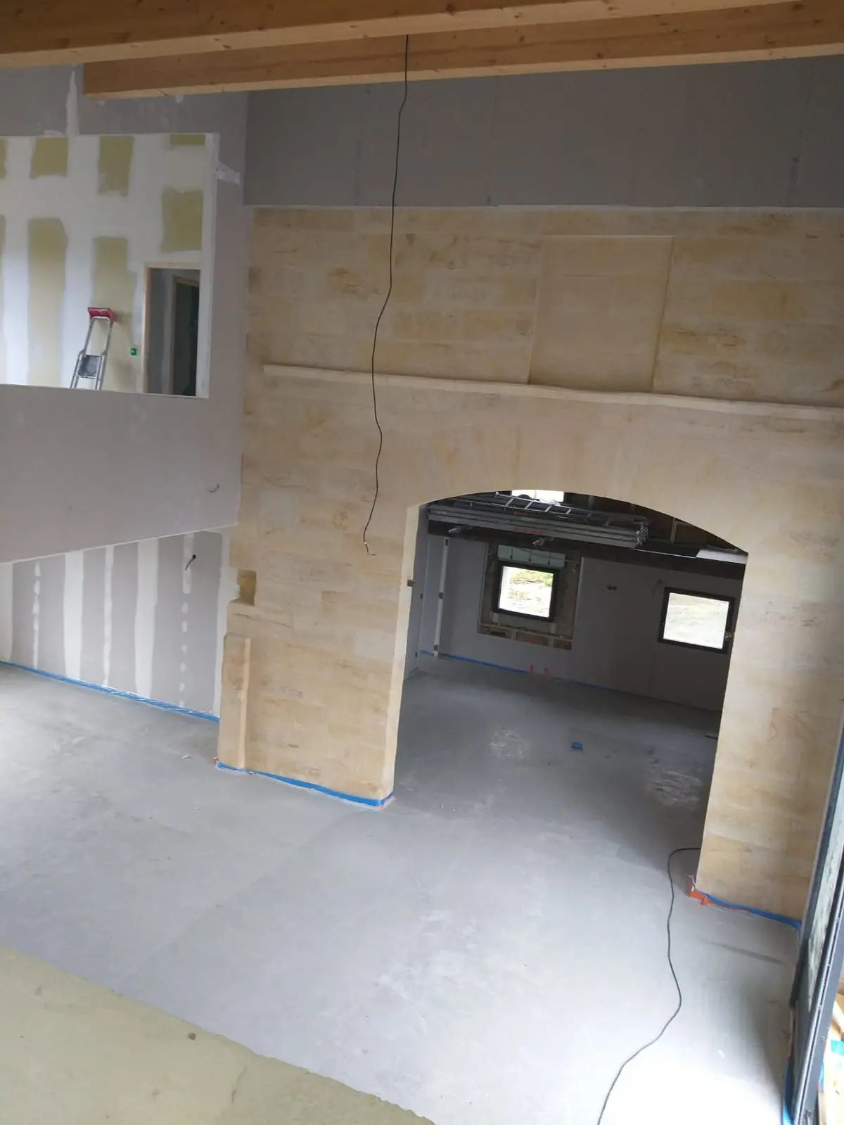 Avant peinture : mur en pierre de taille percé d’une arche, cloisons en plaques de plâtre jointées et sol brut, vus depuis la mezzanine