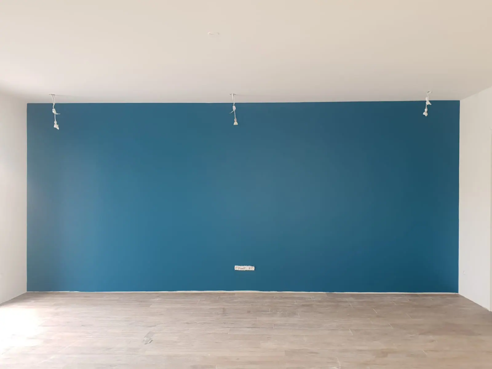 Mur d’accent peint en bleu canard entre des murs et un plafond blancs, sol clair façon parquet