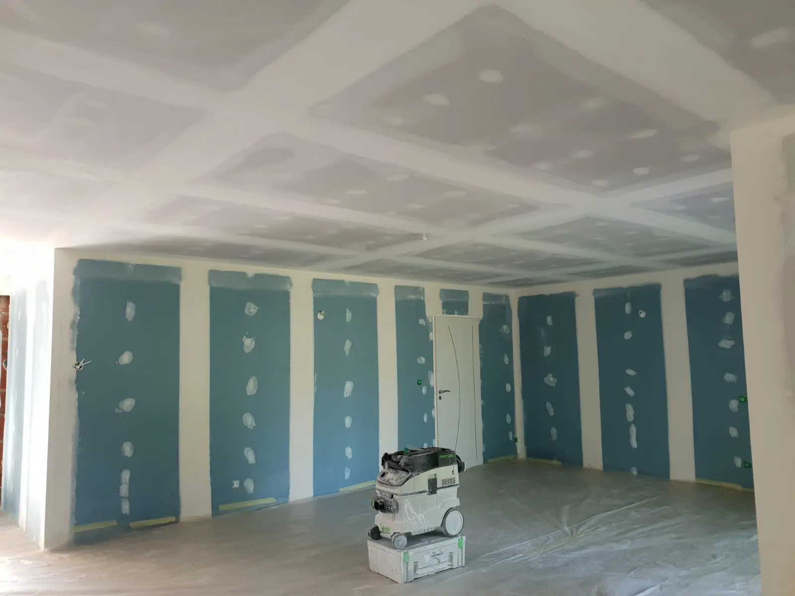 Aspirateur de chantier dans une pièce aux plaques de plâtre jointées, sol protégé par une bâche