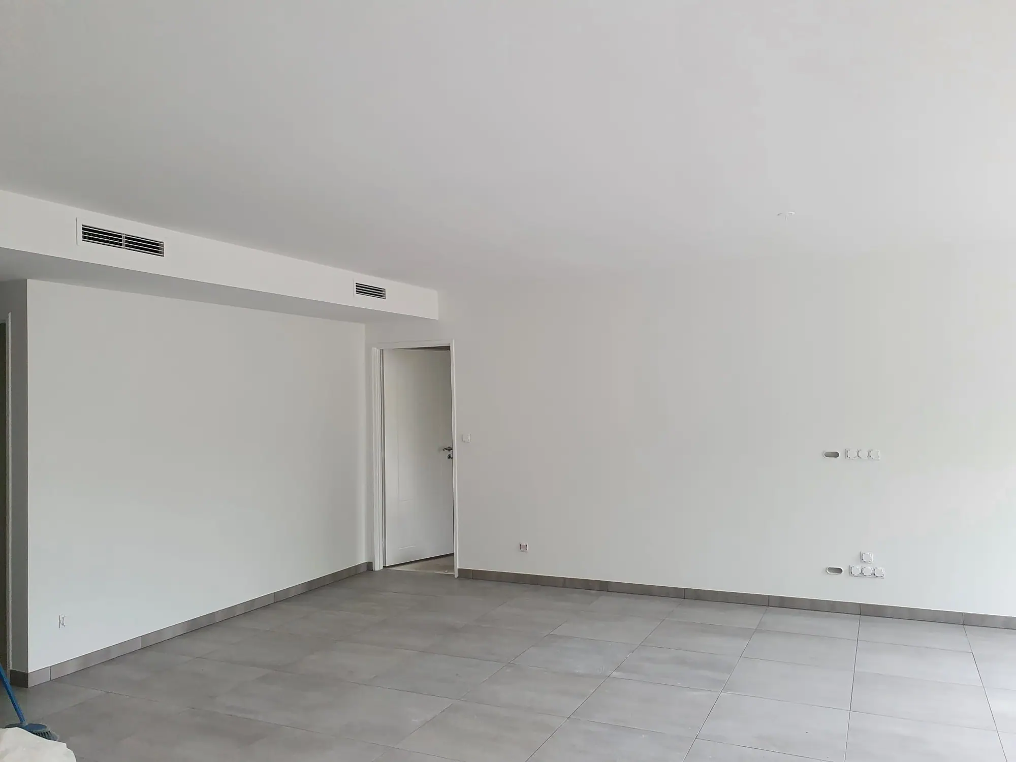 Pièce vide aux murs et au plafond peints en blanc, caisson de climatisation et carrelage gris grand format