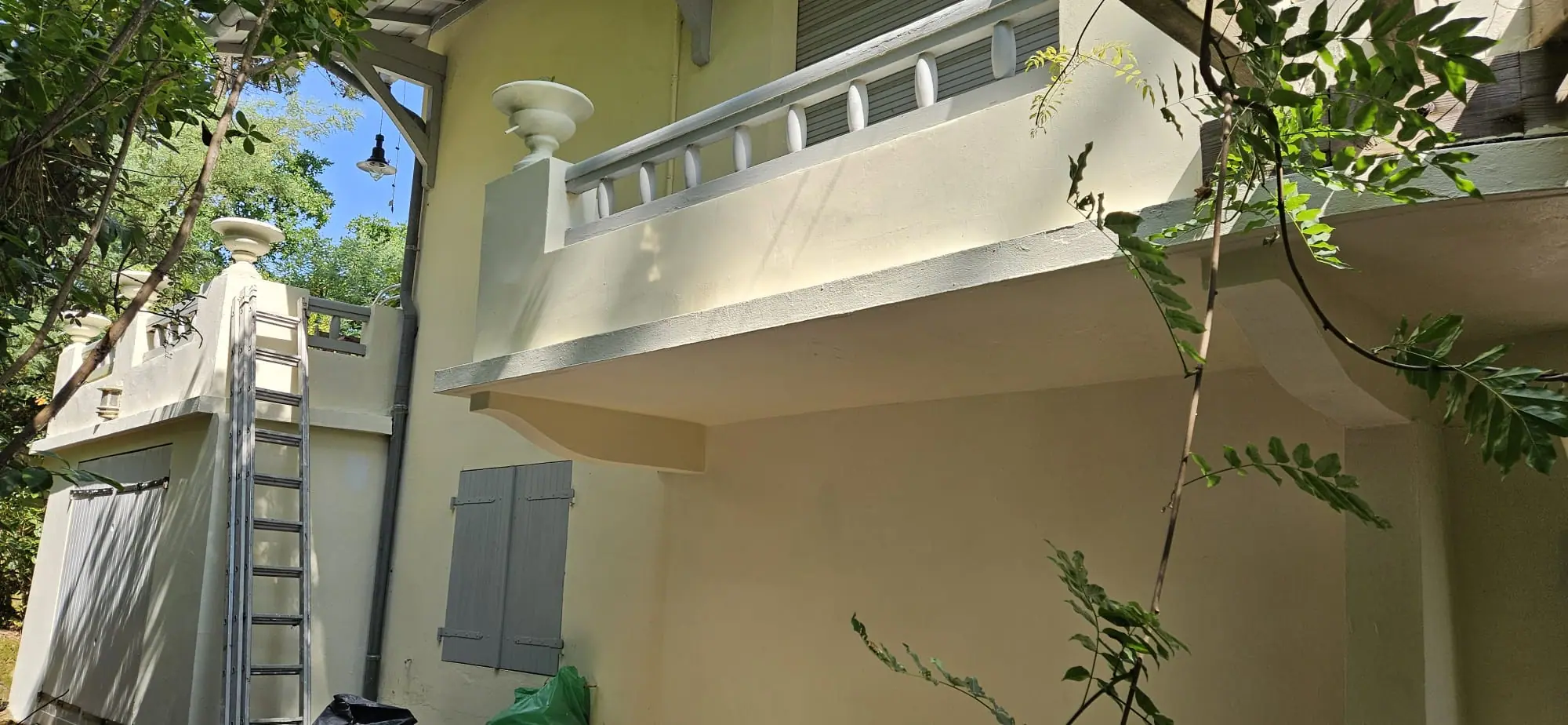 Façade crème d’une villa : balcon à balustres sur consoles, vasque sur pilier et volets gris