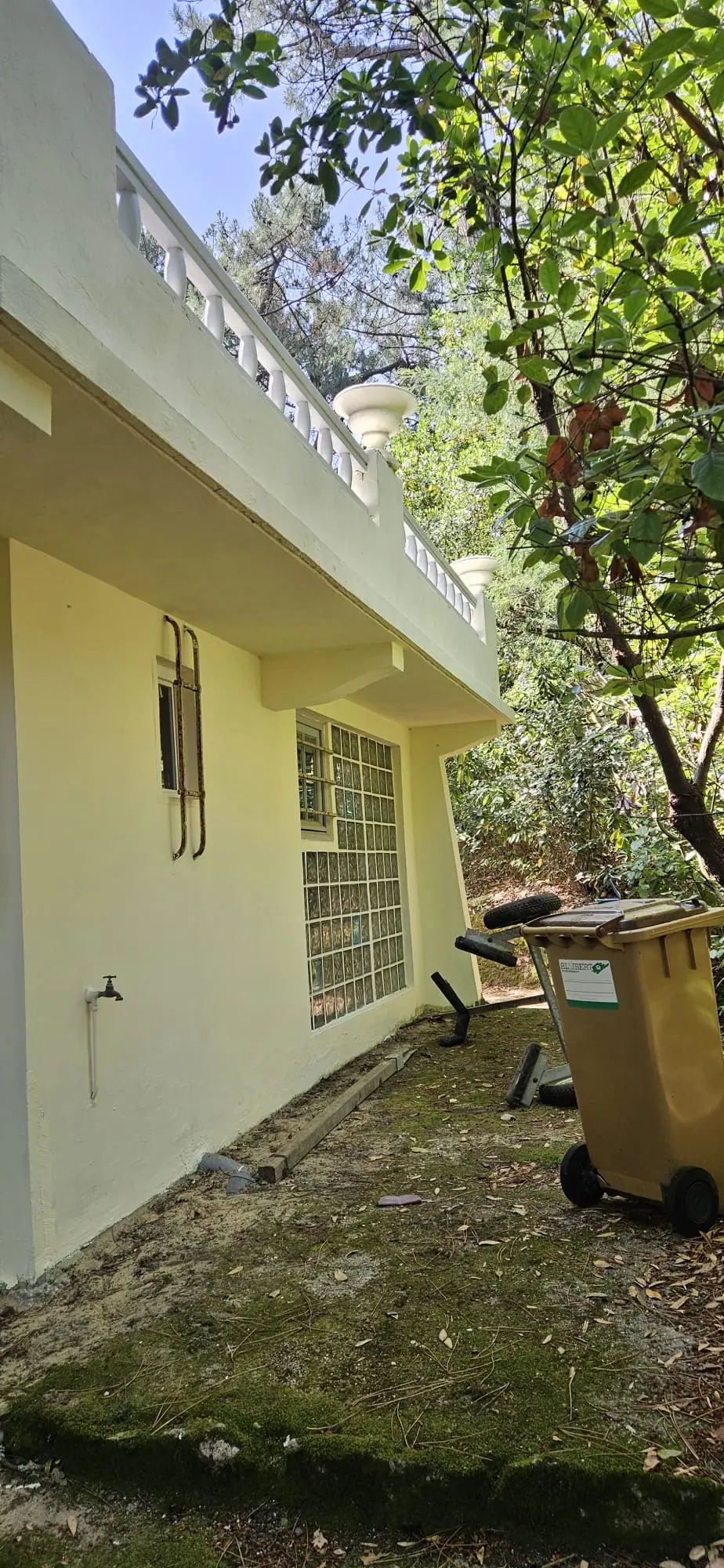 Façade latérale d’une villa peinte en crème, sous une terrasse à balustres et vasques