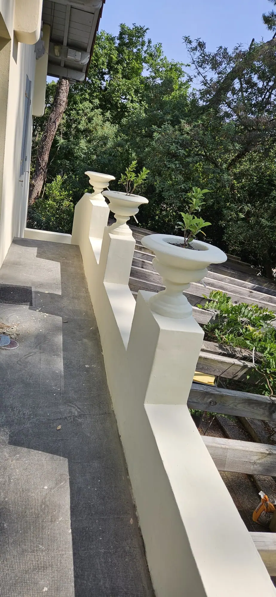 Terrasse bordée d’un muret crème à piliers en escalier surmontés de vasques, au-dessus d’une pergola en bois